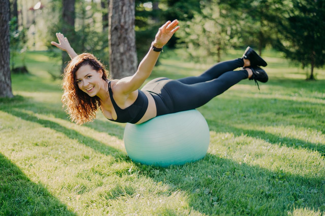 Woman balancing on her stomach outdoors on a yoga ball